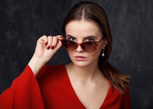 Woman is looking over the sunglasses, gray background