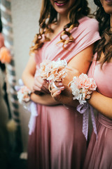Beautiful elegant slim bridesmaids in delicate pink beige summer dress with bracelets of the luxury fresh roses on the wedding ceremony