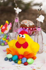 Накрытый для празднования Пасхи стол с крашеными разноцветными пасхальными яйцами, пасхальным куличом, игрушечной желтой курицей и пасхальным декором 