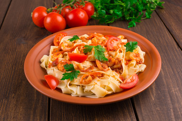 Fettuccine pasta with shrimp tomatoes and herbs. wooden background