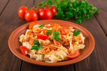 Fettuccine pasta with shrimp tomatoes and herbs. wooden background