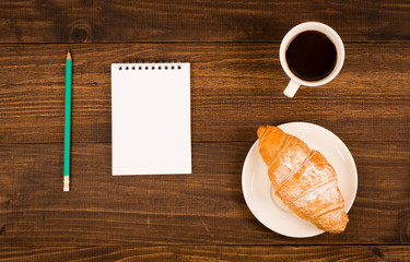 breakfast with cup of black coffee, croissants, notebook with a pen