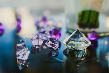 Diamond (small purple jewel) stones heap over mirror glass table, crystal stones, shiny gold and silver jewelery on a table