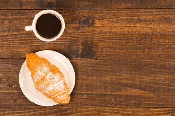 Coffee cup with croissant for breakfast on a dark wooden table, top view.