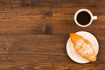 Coffee cup with croissant for breakfast on a dark wooden table, top view.