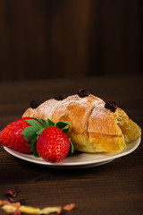 A cup of black tea with dry fruits, croissant with strawberry and wooden table background