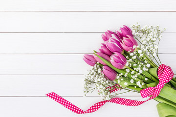 Bouquet of bright pink tulips and gipsophila decorated with ribbon on white wooden background. Top view, copy space