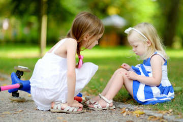Little girl comforting her sister after she fell while riding her scooter