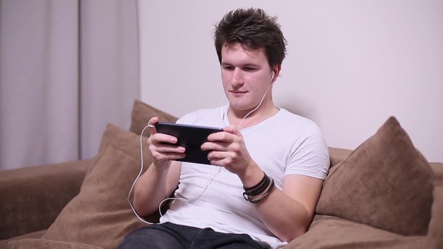 Brunette guy watching a video on the tablet while sitting on a sofa