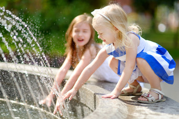 Two cute little girls playing with a city fountain on hot summer day