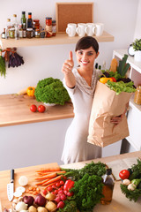 Young woman holding grocery shopping bag with vegetables Standing in the kitchen and showing ok