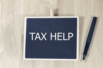 sentence tax help written with chalk on a blackboard, on a table with pen