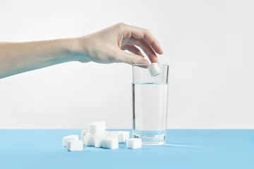 Fotobehang Glass of water against sugar, diabetes disease, sweet addiction, hand drop a sugar © olgapogorelova