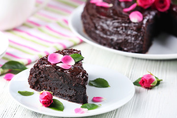 Piece of chocolate cake decorated with flowers on white wooden table