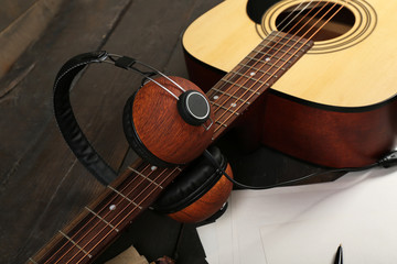 Fototapeta premium Acoustic guitar, headphones, musical notes and white papers on wooden background, close up