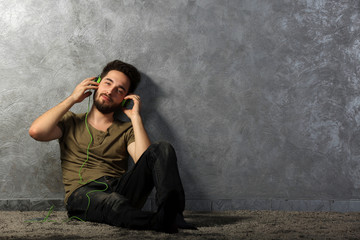 Obraz na płótnie Canvas Young bearded man listens music with headphones sitting on grey wall background