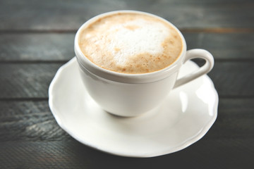 Cup of hot cappuccino with froth on a black wooden table