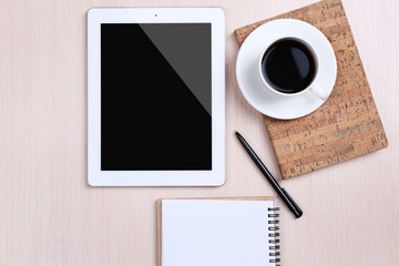 Tablet with cup of coffee and notepad on wooden table