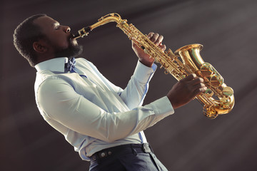 Naklejka na ściany i meble African American jazz musician playing the saxophone on grey background