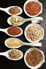 Different kinds of seeds in spoons on wooden table