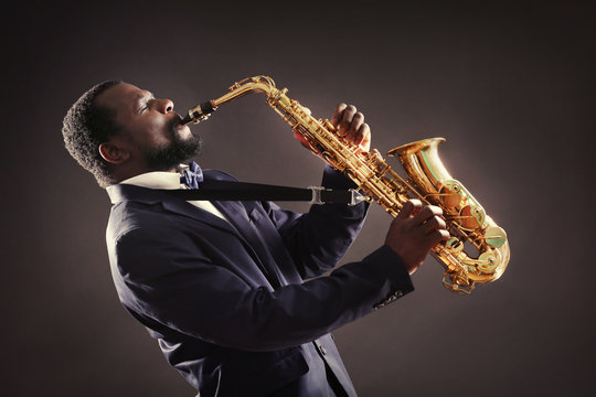 African American jazz musician playing the saxophone on grey background