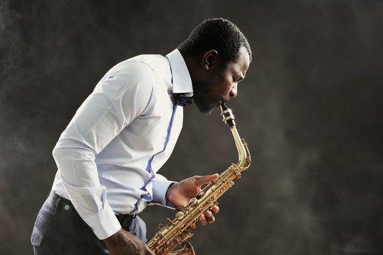 African American jazz musician playing the saxophone on grey background