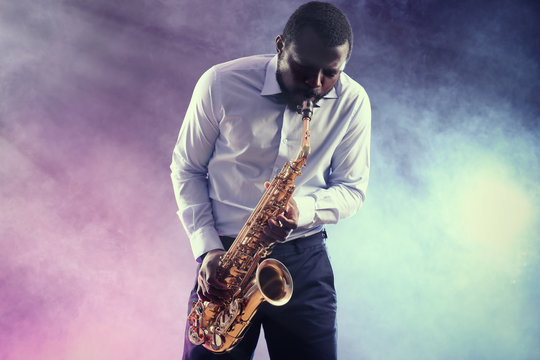 African American jazz musician playing the saxophone against colorful smoky background
