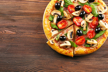 Sliced delicious tasty pizza with vegetables on wooden table