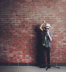 Little boy singing with microphone on a brick wall background