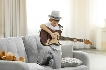 Little boy playing guitar on a sofa at home