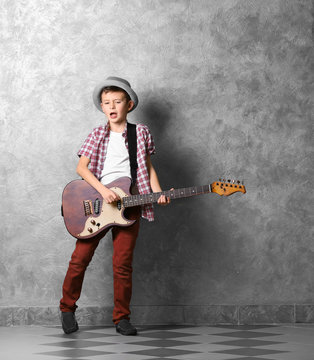 Little boy playing guitar on a grey wall background