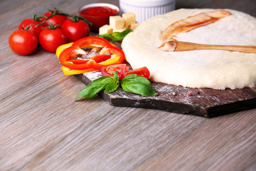 Fresh dough prepared for pizza with tomatoes and sliced pepper on a wooden board, close up