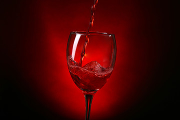 Wine pouring in glass on dark red background
