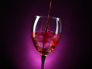 Wine pouring in glass on dark purple background