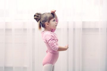 Little cute girl in pink leotard making new ballet movement at dance studio