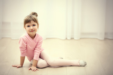 Naklejka premium Little cute girl in pink leotard sitting on floor at dance studio