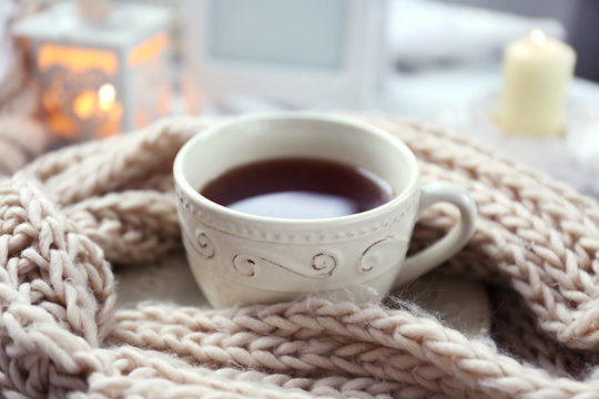 Cup of tea and knitted scarf on coffee table in the room, close up