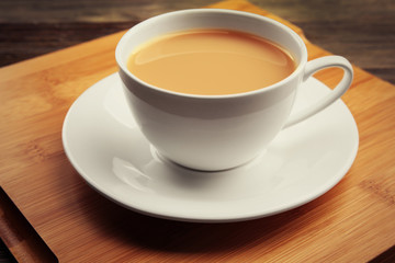 Porcelain cup of tea with milk on wooden tray, close up