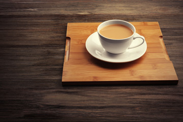Porcelain cup of tea with milk on wooden tray, close up