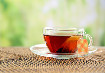Black tea with bag in glass cup on green blurred background, close up