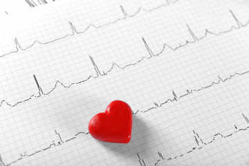 Cardiogram chart with small red heart on table closeup