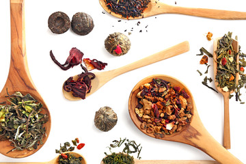 Different sorts of dry tea in wooden spoons, isolated on white