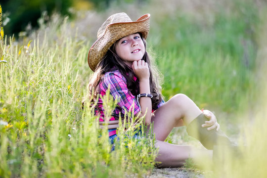 little girl sitting in a field wearing a cowboy hat