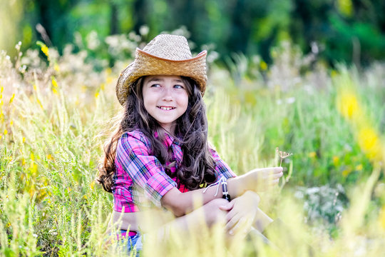 little girl sitting in a field wearing a cowboy hat