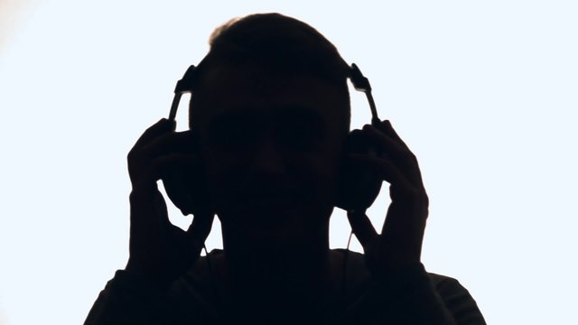 Young guy listening to music on headphones and dancing to the rhythm. It is backlit. DJ silhouette.