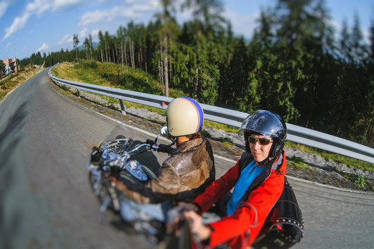 Young man biker riding his motorcycle on the road with the passenger. Biker is wearing leather jacket helmet and sunglasses. Selfie style picture. Motion picture. Tilt shift lens blur effect