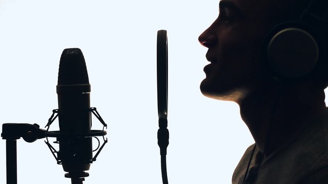 The guy sings hip hop in the recording studio. Man records a song.