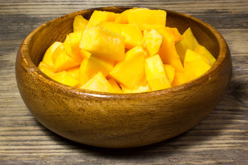 The cubes of pumpkin in wooden plate on wooden background