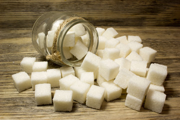 Sugar cubes in glass jar on wooden background