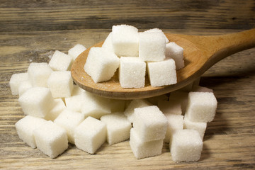 Cubes of Sugar in wooden spoon on wooden background